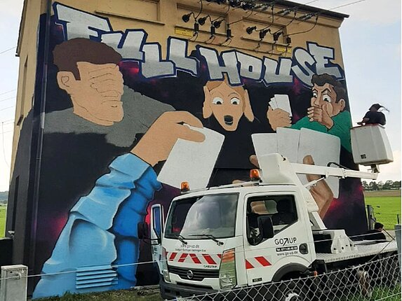 Schaltanlage zwischen Darmsheim und Ehningen Motiv des Graffitis: Mehrere Personen, Hände, weisse Spielkarten und die Worte "Full House" sind zu erkennen. Ein Auto mit Hebebühne steht vor dem Gebäude.