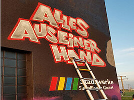 An einer Hauswand stehen die Worte "Alles aus einer Hand" und das Logo der Stadtwerke Sindelfingen. Eine Leiter lehnt an der Hauswand.
