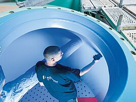 Ein Mitarbeiter steht in einem leeren Wassertank und hält ein Messgerät an die Wand. Ein Baugerüst ist um diesen Tank aufgebaut.