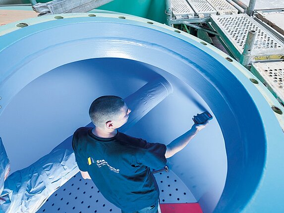 Ein Mitarbeiter steht in einem leeren Wassertank und hält ein Messgerät an die Wand. Ein Baugerüst ist um diesen Tank aufgebaut.