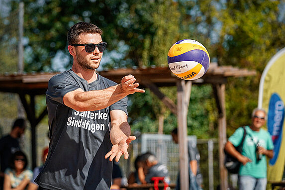 Nahaufnahme eines Volleyballspielers mit Sonnenbrille. Der gespielte Volleyball vor ihm in der Luft.