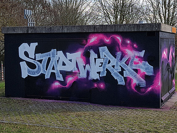 Ein technisches Gebäudes ist mit einem Graffiti verschönert. Besprüht mit den Worten "Stadtwerke Sindelfingen", sowie rosafarbene Blitze auf schwarzem Grund.