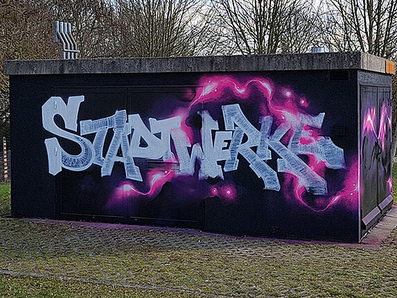 Ein technisches Gebäudes ist mit einem Graffiti verschönert. Besprüht mit den Worten "Stadtwerke Sindelfingen", sowie rosafarbene Blitze auf schwarzem Grund.