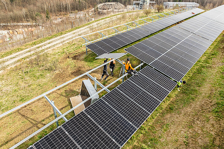 Luftaufnahme der Bauarbeiten an der Fotovoltaikanlage. Einige Arbeiter bringen die Solarpanels an die vorgesehene Konstruktion an.