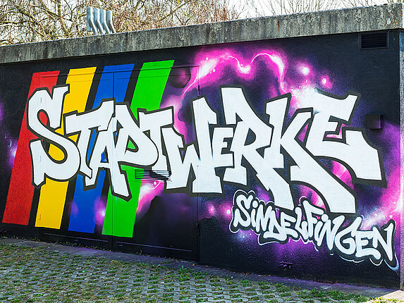 Ein technisches Gebäudes ist mit einem Graffiti verschönert. Besprüht mit den Worten "Stadtwerke Sindelfingen", sowie rosafarbene Blitze auf schwarzem Grund.