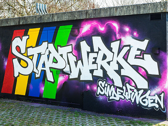 Ein technisches Gebäudes ist mit einem Graffiti verschönert. Besprüht mit den Worten "Stadtwerke Sindelfingen", sowie rosafarbene Blitze auf schwarzem Grund.