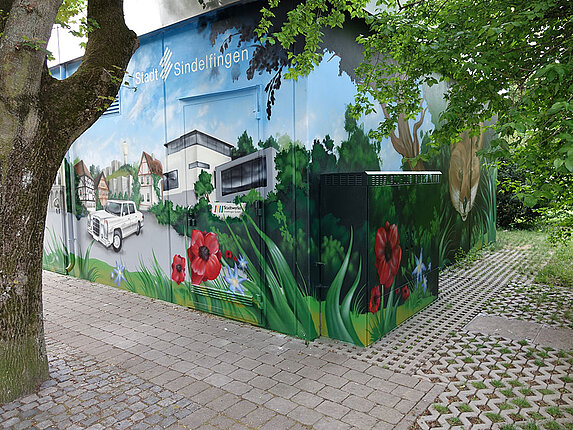 Ein technisches Gebäude mit einem grossflächigen Graffiti. Das Motiv: Der Marktplatz von Sindelfingen, umrahmt von grossen Bäumen und Blumen.