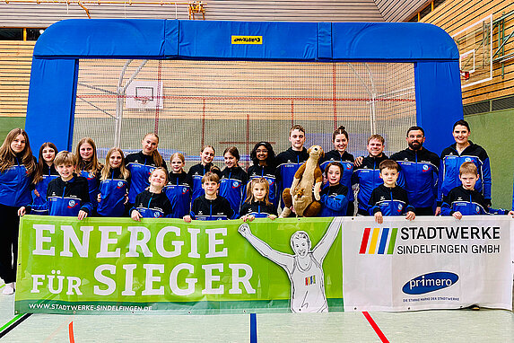 Turngruppe des VfL Sindelfingen, im Hintergrund steht das Trampolin. Im Vordergrund halten die Jugendlichen das Banner der Stadtwerke Sindelfingen mit der Aufschrift Energie für Sieger