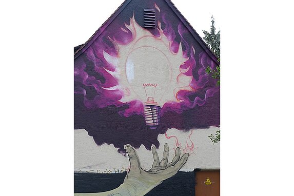 Das Graffiti zeigt eine grosse leuchtende Glühbirne, rosafarbene Blitze gehen von ihr aus. Eine ausgestreckte Hand ist darunter zu sehen.