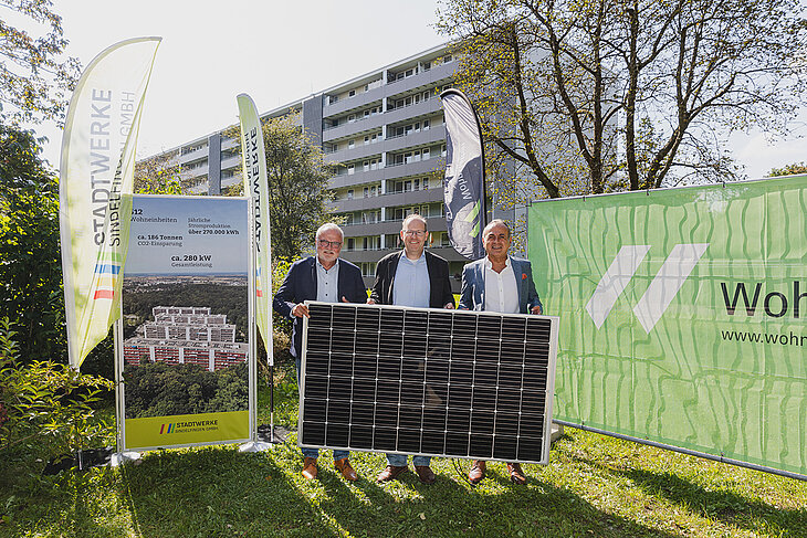 Pressefoto mit dem Oberbürgermeister, dem Geschäftsführer der Stadtwerke Sindelfingen und dem Geschäftsführer der Wohnstätten der Watzmannstraße. Alle drei stehen draußen vor einem der Plattenbauten und halten gemeinsam ein Solarpanel in den Händen.