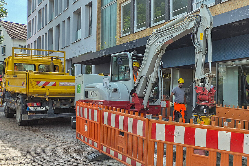 Eine Baustelle mit einem LKW im Hintergrund und einem Elektrobagger, der einen Graben aushebt