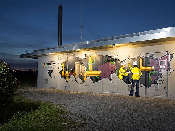 Gasdruckregelstation in der Rudolf-Harbig-Straße Nahaufnahme eines Graffitis bei Nacht: Es scheint als wäre die Hauswand aufgebrochen und man können in das Innere des Gebäudes schauen.Zwei Baurbeiter in gelber Sicherheitsjacke und mit Bauhelm befinden sich zwischen vielen Rohren und technischen Anlagen.