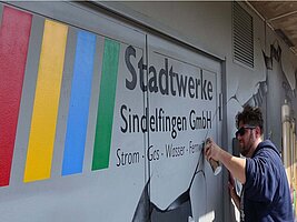 Der Graffiti-Künstler bei der Arbeit. Er setzt die Spraydose ganz nah an die Hauswand und zieht eine dünne Linie.