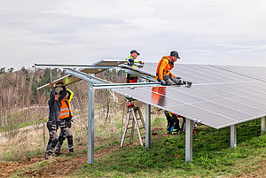 Mehrere Bauarbeiter befestigen ein Solarpanel auf die dafür vorgesehenen Stangen.