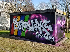Ein technisches Gebäudes ist mit einem Graffiti verschönert. Besprüht mit den Worten "Stadtwerke Sindelfingen", sowie rosafarbene Blitze auf schwarzem Grund.