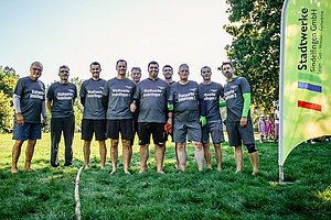 Teamfoto einiger Männer in gleichen Trikots auf einer grünen Wiese. Im Gras liegt ein dickes Tauseil, daneben steht ein Banner der Stadtwerke Sindelfingen.