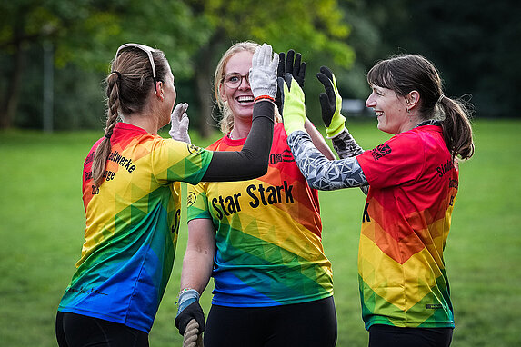 Drei Frauen klatschen sich ab. Sie stehen auf der Wiese beim Tauziehen während der Stadtwerke Teamchallenge