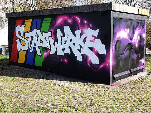 Ein technisches Gebäudes ist mit einem Graffiti verschönert. Besprüht mit den Worten "Stadtwerke Sindelfingen", sowie rosafarbene Blitze auf schwarzem Grund.