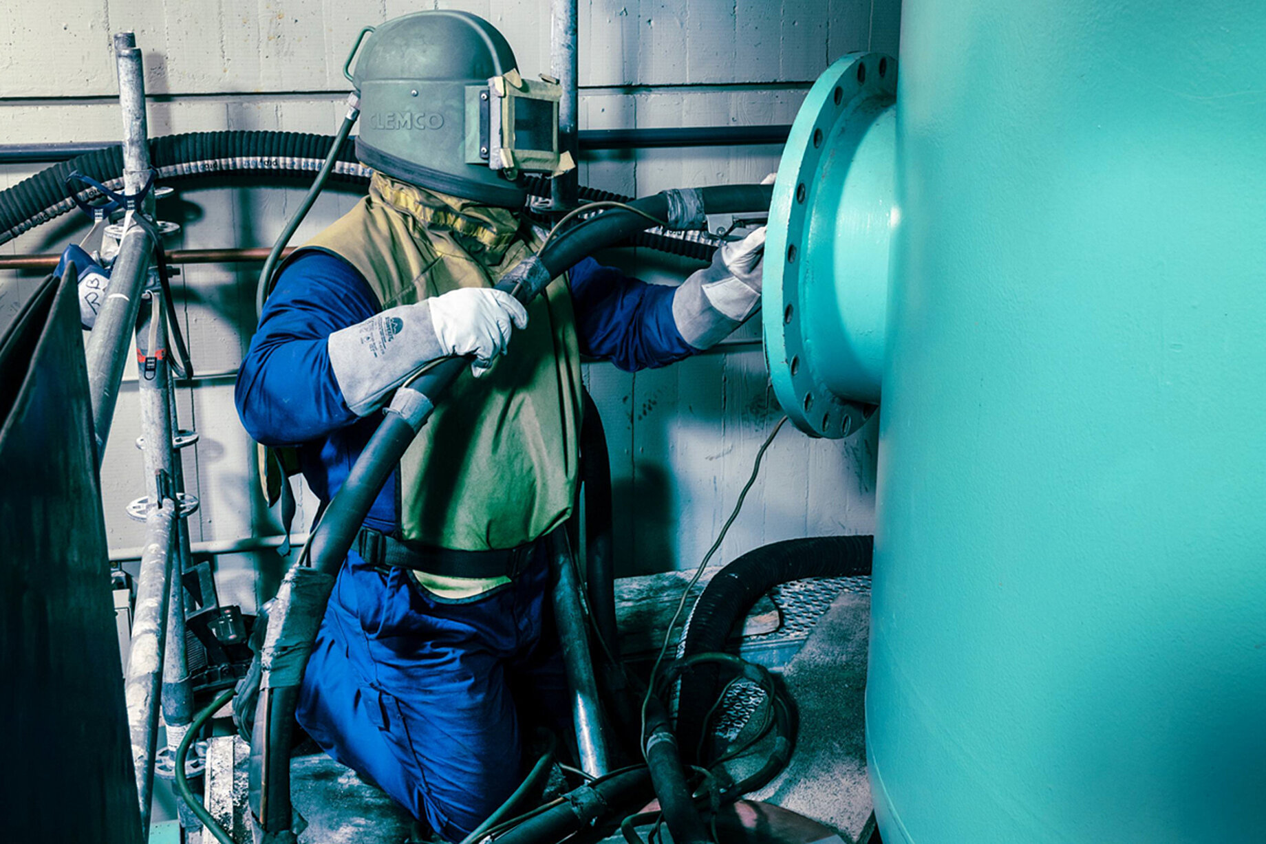 Ein Mitarbeiter in einem Schutzanzug und Maske reinigt mit einem Schlauch eine Anlage im Filterwerk