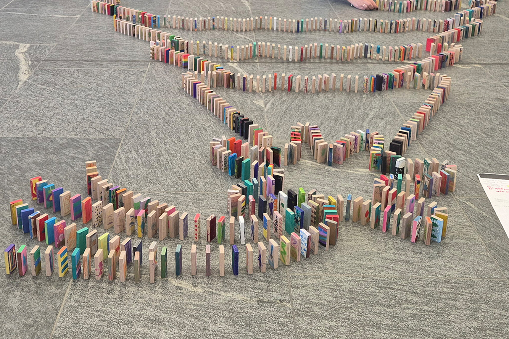 Unzählige bemalten Holzsteine oder Dominosteine stehen hintereinander aufgestellt auf dem Fußboden.