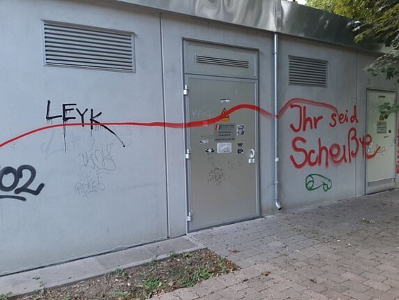 Ein graues technisches Gebäude ist unschön mit Graffities beschmiert.