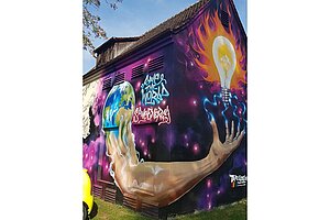 Ein Haus mit einem großflächigen Graffiti. Motiv des Graffitis: Aus der Erdkugel wächst ein Arm heraus. Die Finger sind nach oben gespreizt und blaue Blitze führen zu einer Glühbirne. Diese leuchtet hellgelb, drumherum sind orangefarbene Flammen. Die Worte "Save the World" und "Save Energy" stehen zusätzlich neben der Erdkugel.