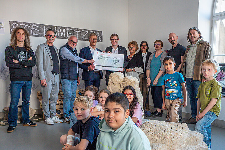 Die Vertreter von kidsatkita, Stadt Sindelfingen, Stadtwerke Sindelfingen sowie die Künstler halten den Scheck der Stadtwerke in der Hand. Im Vordergrund sind die Kinder zu sehen.