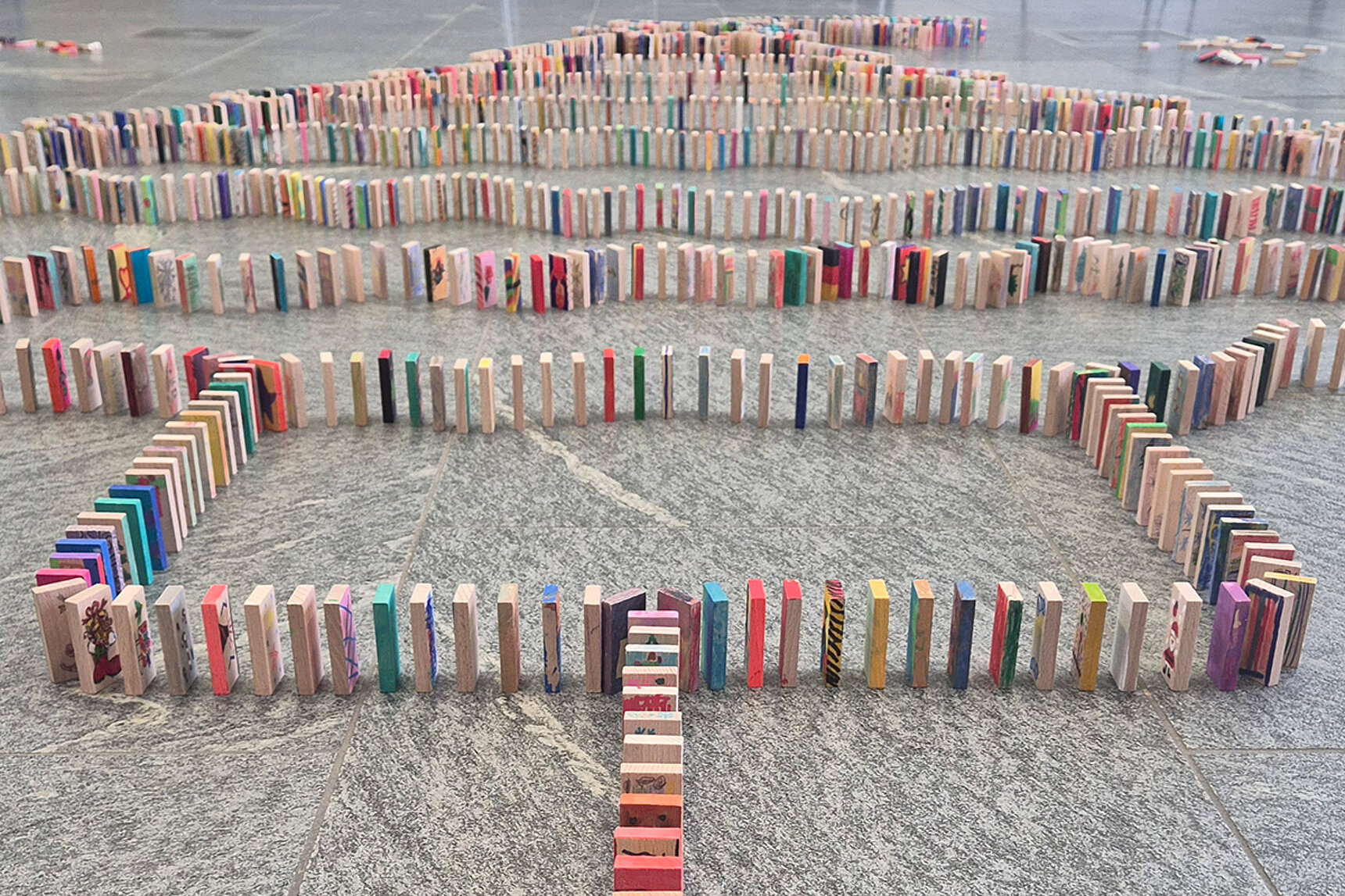 Unzählige bemalten Holzsteine oder Dominosteine stehen hintereinander aufgestellt auf dem Fußboden.