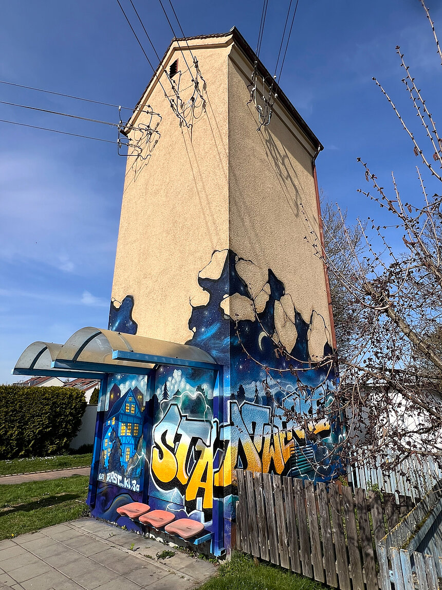 An einem Stationsgebäude der Stadtwerke ist ein Graffiti angebracht. Darauf zu sehen ist ein beleuchtetes Haus bei Nacht, das Wort Stadtwerke, Mond und Sterne