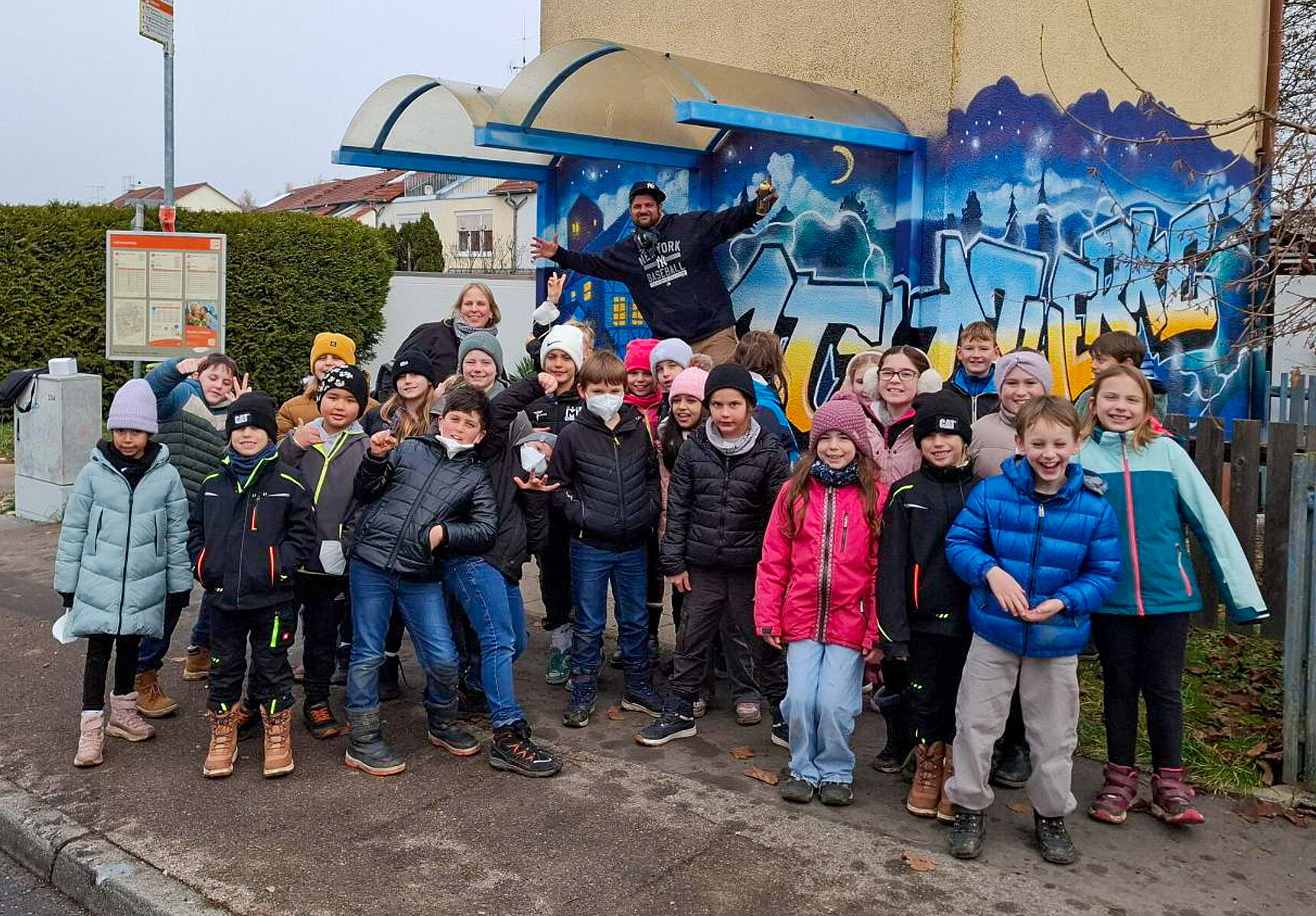 Graffiti-Künstler Max Frank steht mit einer Schulkasse vor der mit Graffiti gestalteten Station
