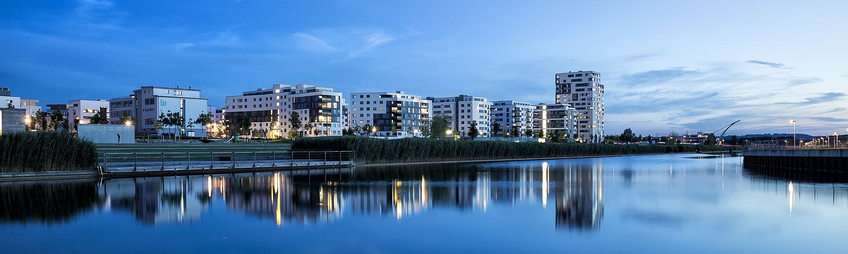 Die Neubauten des Stadtteils Flugfeld in der Abenddämmerung spiegelt sich im Wasser.