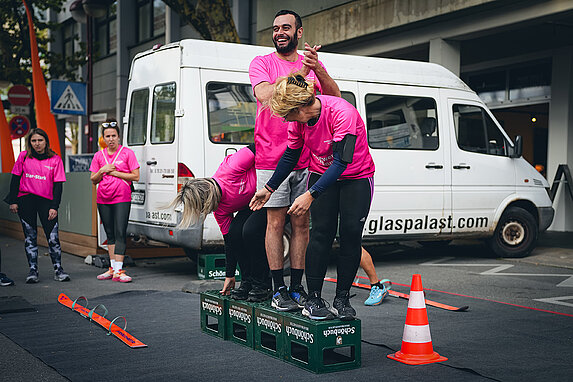 Drei Mitglieder bei der Teamchallenge stapeln Kisten voreinander, auf denen Sie stehen müssen