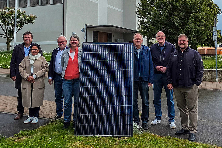 Vertreter/-innen der Kirche, der Stadt Gärtringen und der Stadtwerke Sindelfingen stehen neben einem PV-Modul. Im Hintergrund zu sehen ist die katholische Kirche Gärtringen mit der PV-Anlage auf dem Dach
