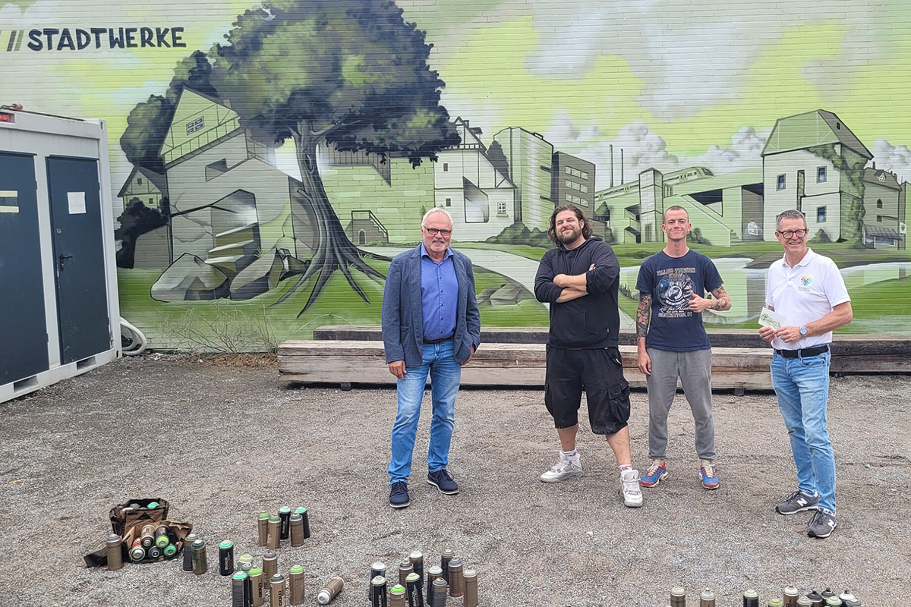 Herr Dr. Hoffmann, Kulturamtsleiter Markus Nau und die Graffiti-Künstler stehen vor dem fertigen Kunstwerk. Das Motiv: Eine Stadtsilhouette in Grüntonen, die einzelnen Gebäude formen das Wort "Sindelfingen".
