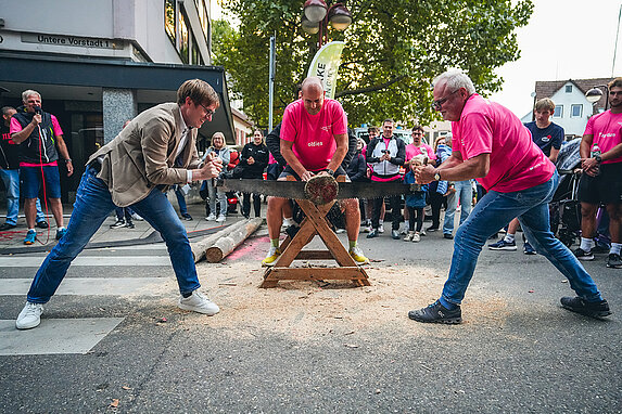 OB Markus Kleemann und Dr. Hoffmann sägen einen Baumstamm durch, Axel Stahl sitzt auf dem Stamm