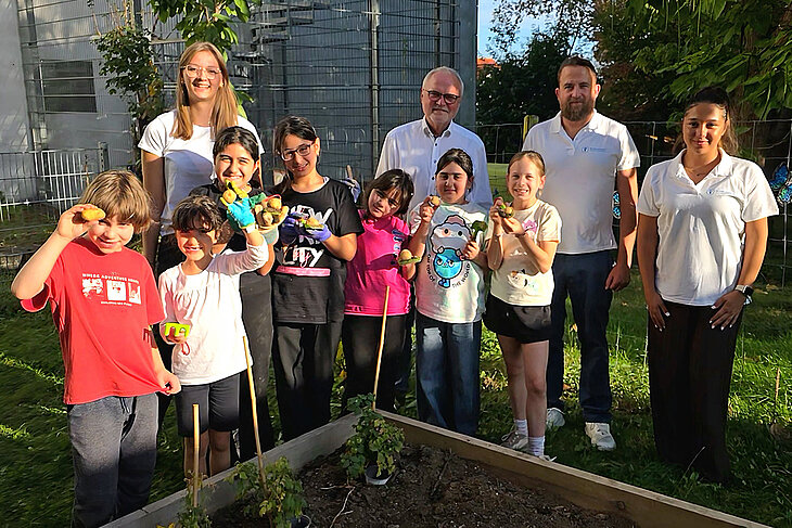 Kinder des Kinderschutzbundes stehen gemeinsam mit Vertretern des Kinderschutzbundes sowie dem Geschäftsführer der Stadtwerke Sindelfingen vor einem Beet, in dem Kartoffeln gepflanzt wurden. Die Kinder halten die geernteten Kartoffel in die Luft