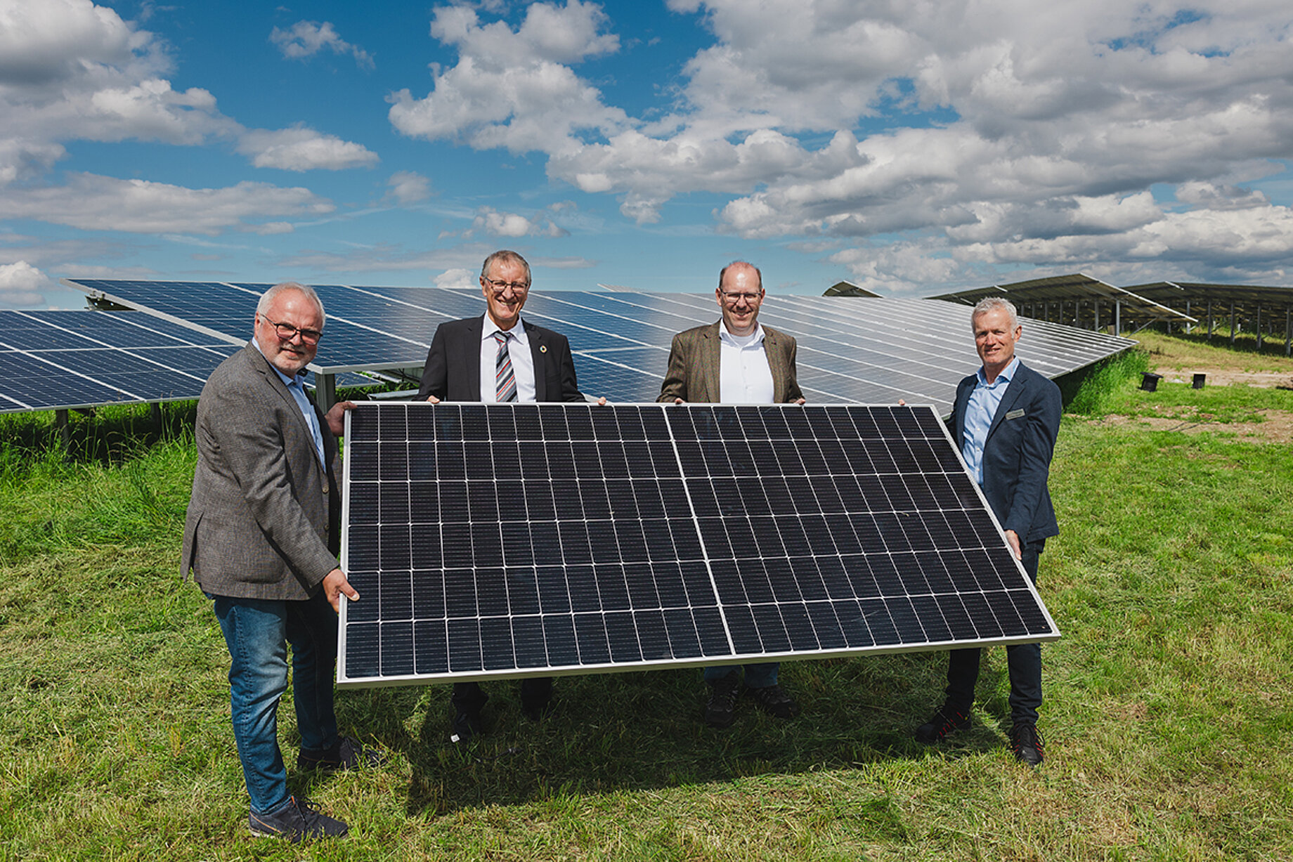 Vier Männer, darunter Herr Hoffmann und der Oberbürgermeister Herr Vöhringer, stehen in einer Fotovoltaikanlage und halten gemeinsam ein Solarpanel in den Händen.