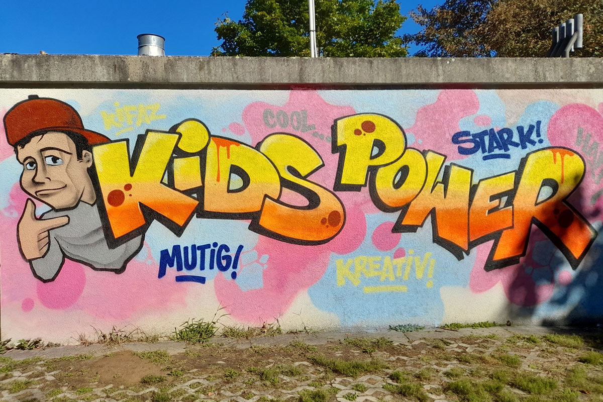 Ein buntes Graffiti an einer Hauswand mit den Worten "Kids Power". Zusätzlich stehen die Worte "mutig", "kreativ", "stark" und "cool" drumherum.