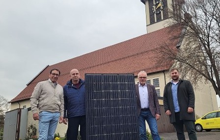 bau-pv-anlage-kirche Pressefoto mit Herrn Dr. Hoffmann und drei weiteren Männern vor der Martinskirche. Ein Solarpanel steht zwischen den Männern.