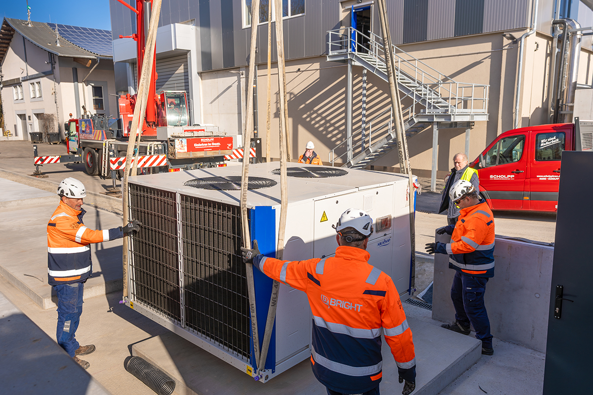 Die neue Biogasanlage wird mit Hilfe eines Krans auf der vorgesehenen Stelle platziert. Vier Baubeteiligte schieben die Anlage in Position.