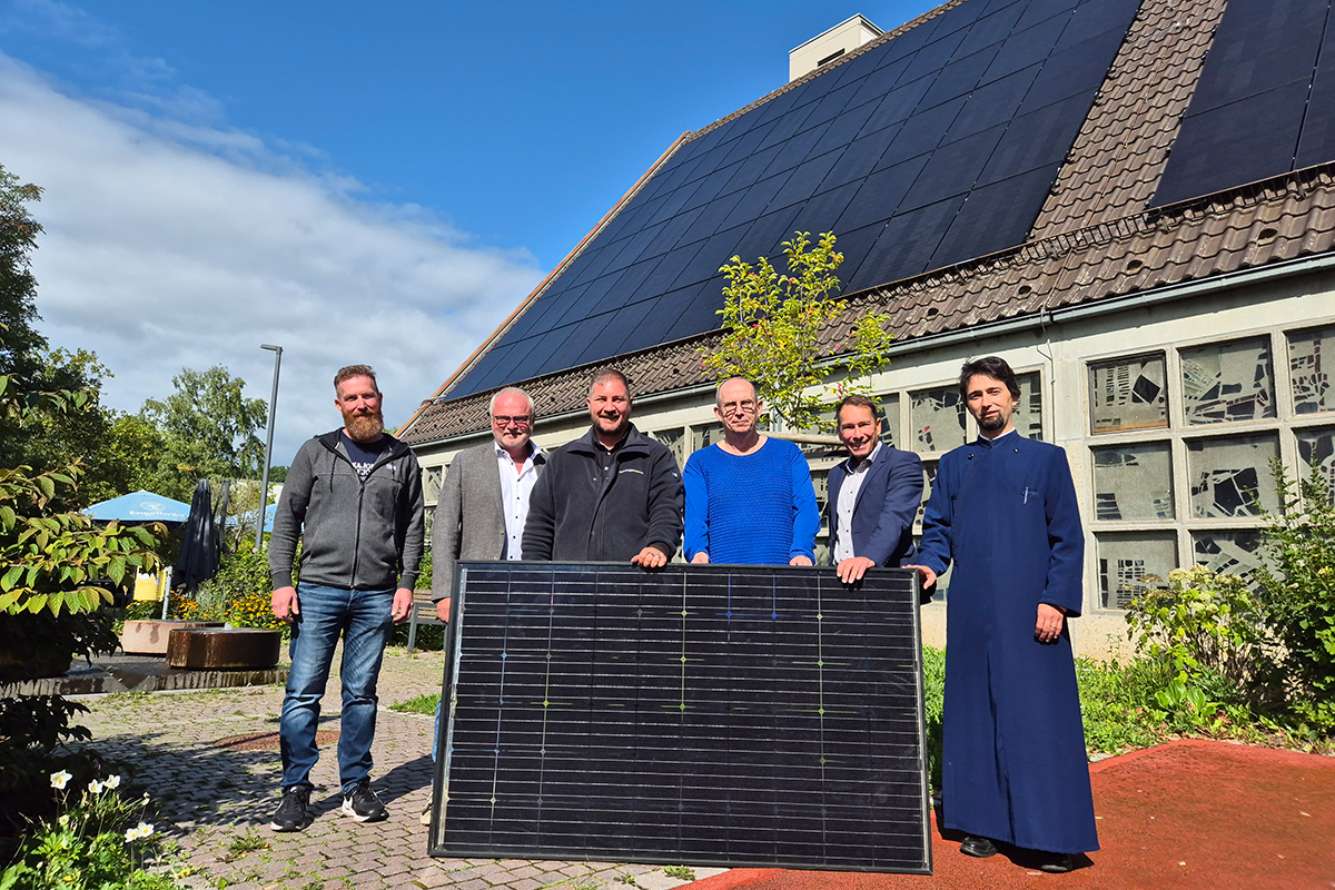 Die Mitarbeiter der Stadtwerke sowie Personen aus der Kirchenverwaltung stehen mit einem PV-Modul vor der Kirche. Auf dem Dach befindet sich eine PV-Analge