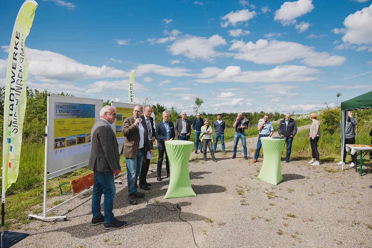 Die Verantwortlichen der Inbetriebnahme der Fotovoltaikanlage geben eine Pressekonferenz. Sie stehen vor Ort vor einigen Erklärtafeln, im Hintergrund ist die Stadt Sindelfingen zu sehen.